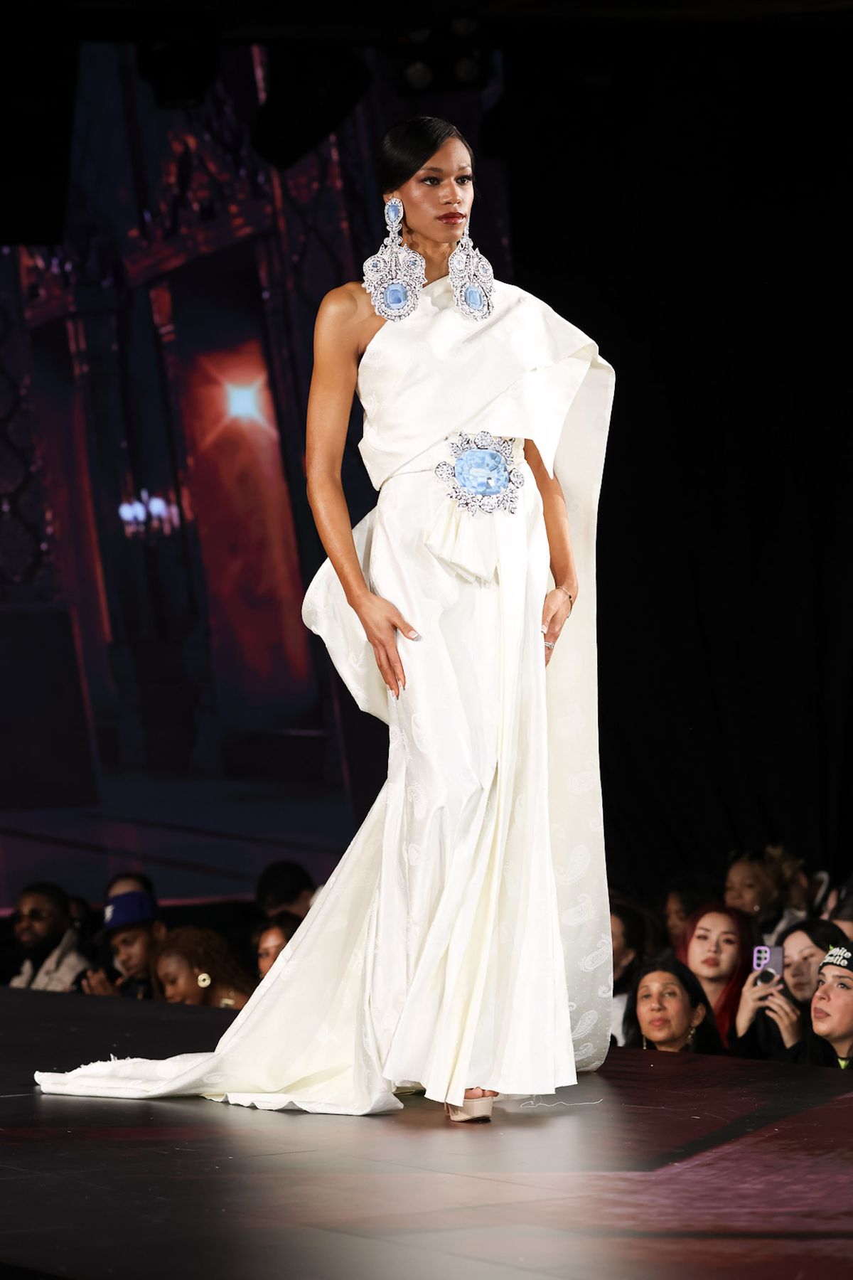 Model in a white gown with blue embellishments on the runway