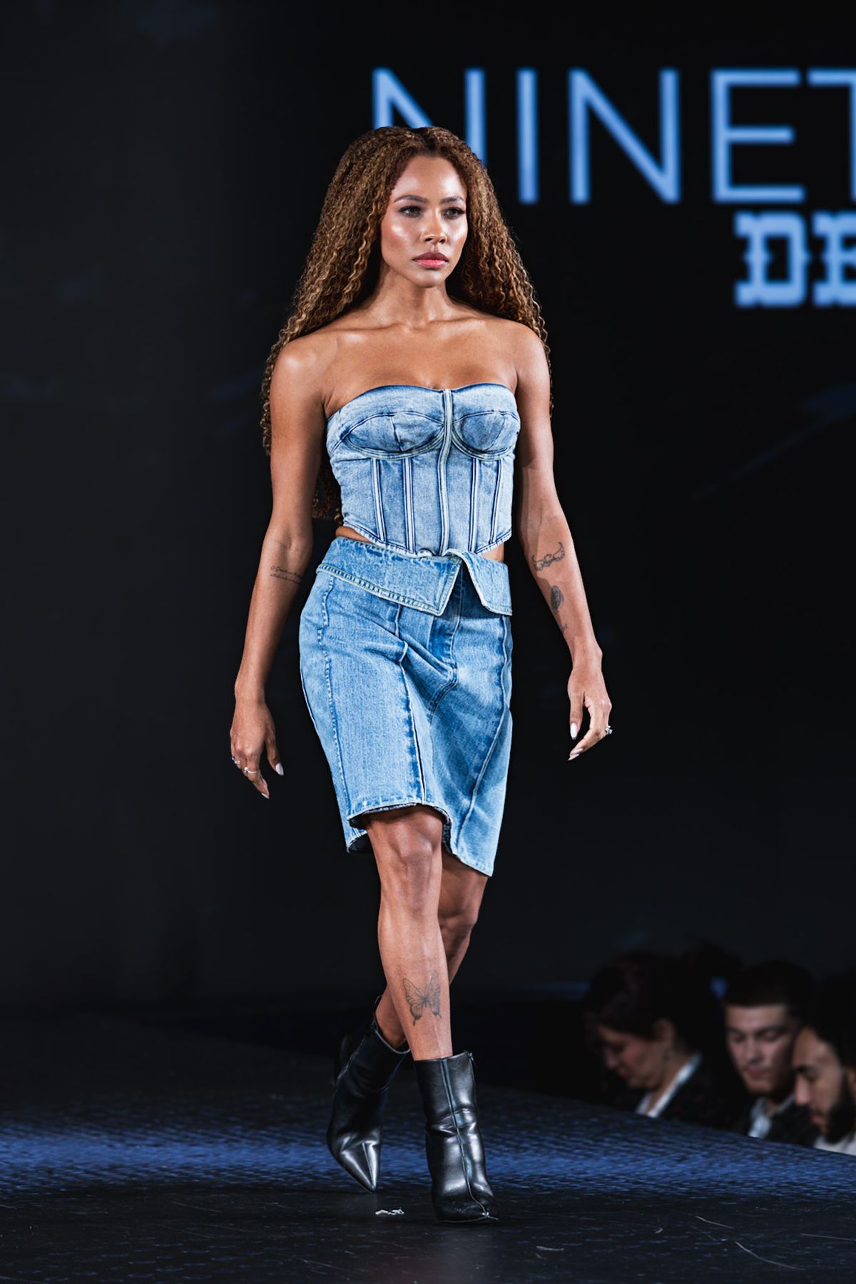 Model in a denim corset top and skirt walking the runway