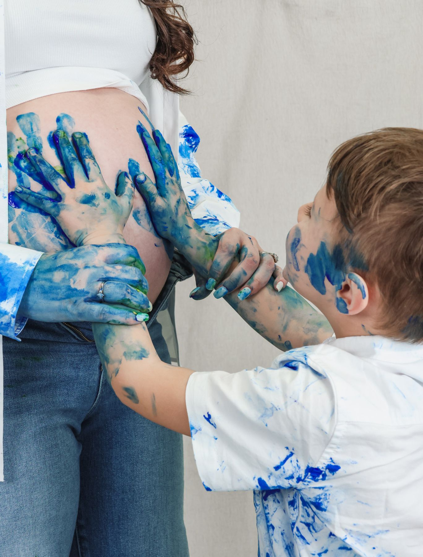 Child and parents adding blue paint handprints to a baby bump