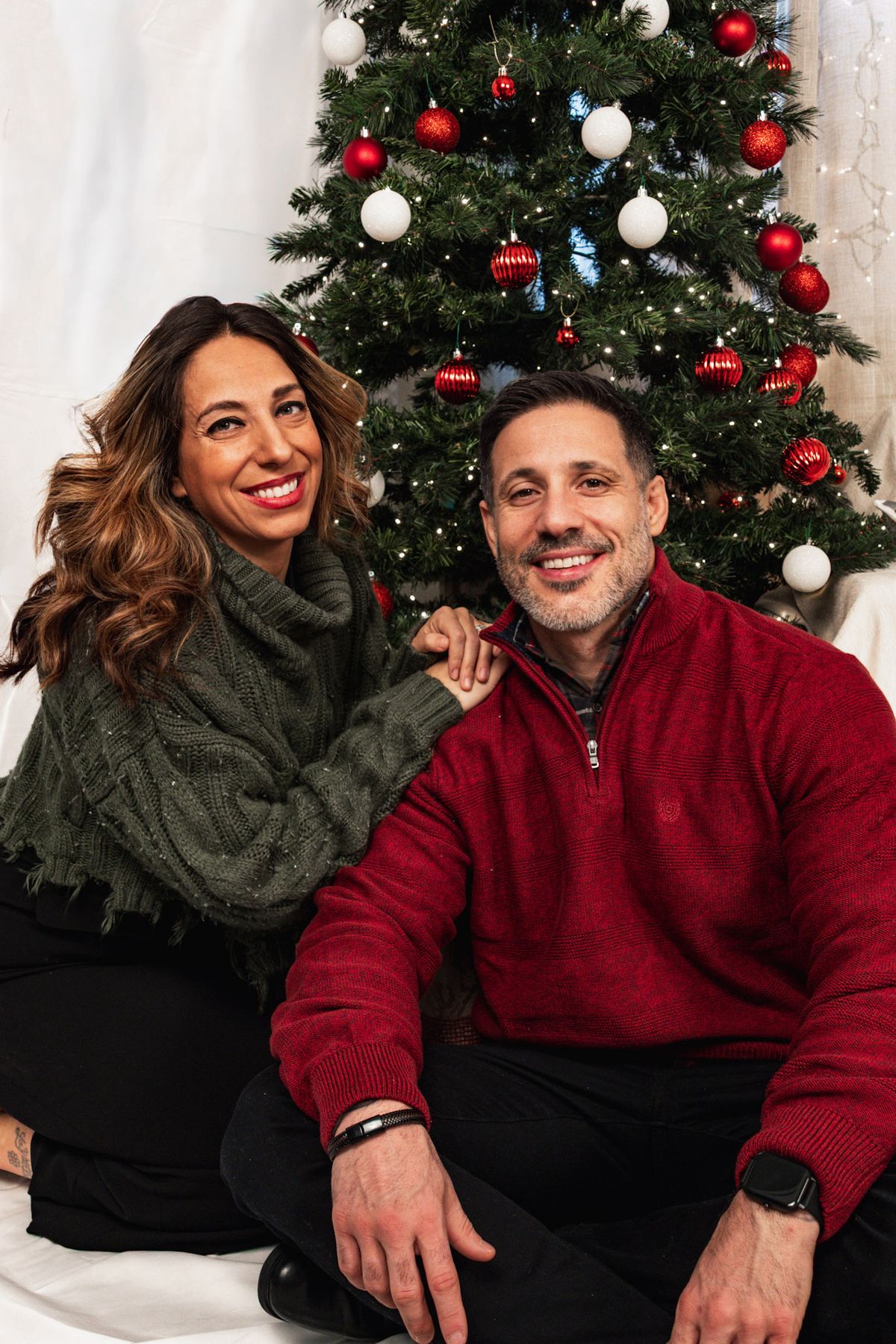 Couple in green and red sweaters posing beside a Christmas tree