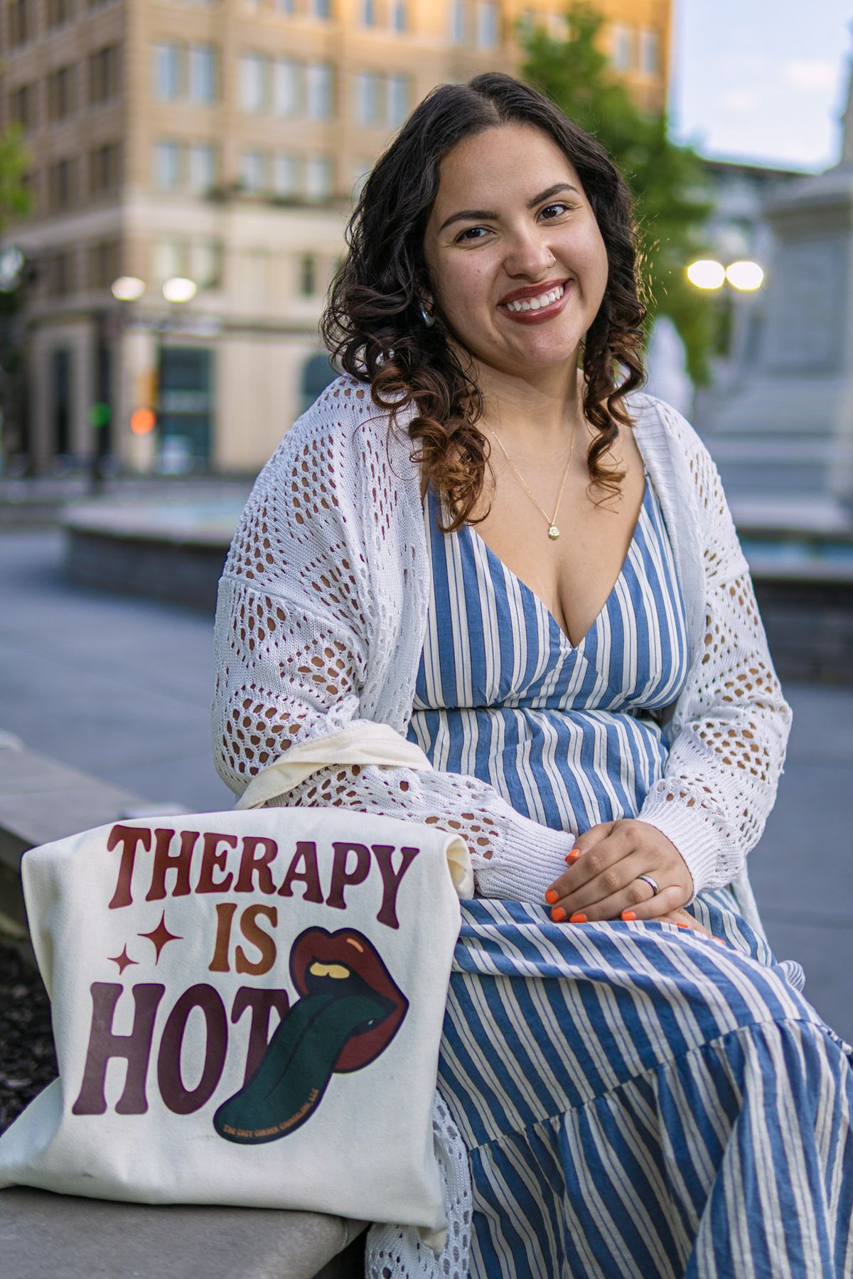 Smiling woman in a blue striped dress sitting outdoors in a city square