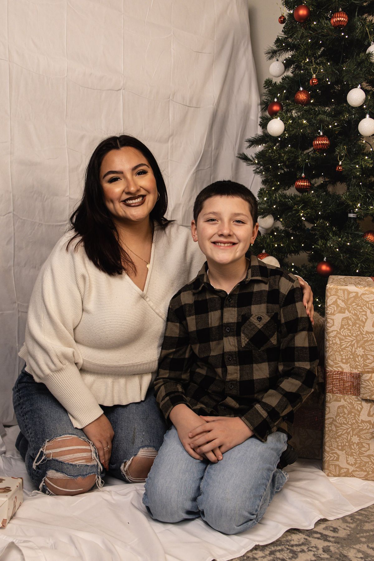 Woman and young boy smiling together in front of a Christmas tree
