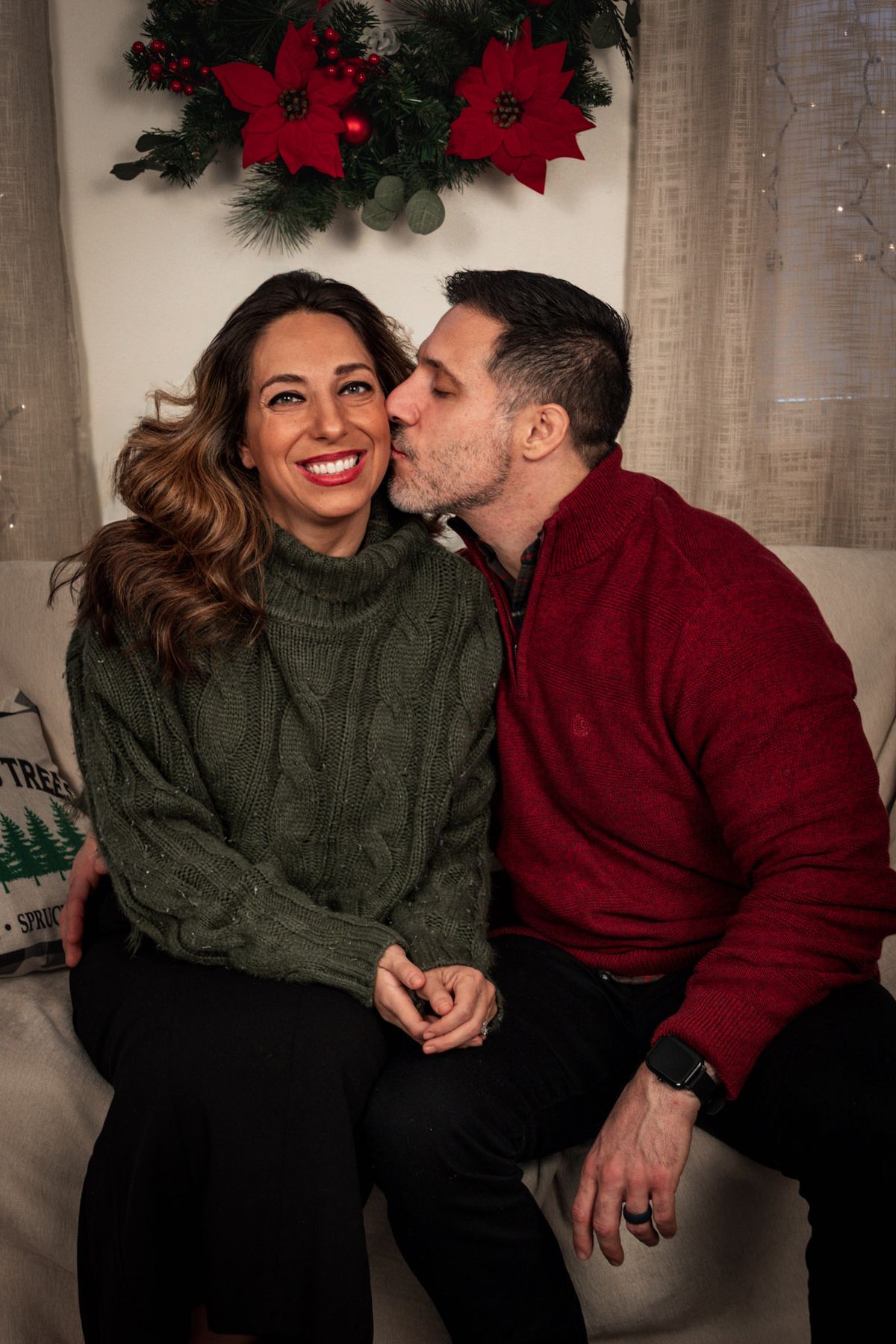 Couple sharing a kiss on the cheek on a couch with holiday decor